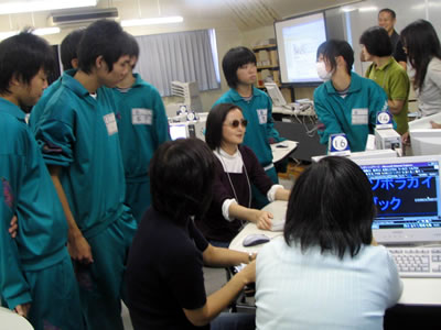 中学生たちにパソコンの操作を説明している岡野さんの写真